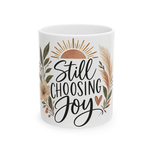 A white ceramic mug featuring the hand-lettered quote 'Still CHOOSING Joy' in black script, surrounded by a warm-toned floral and sun illustration in beige, brown, and muted green on a white background.