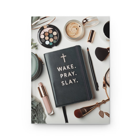 Black notebook with 'Wake. Pray. Slay.' text on a white surface with makeup items.