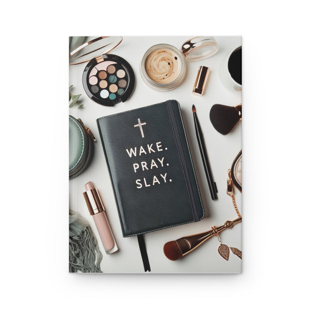 Black notebook with 'Wake. Pray. Slay.' text on a white surface with makeup items.